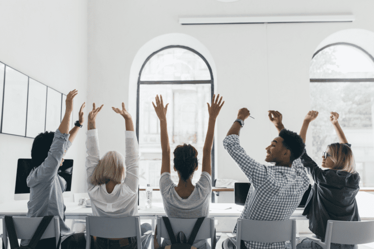 Workers in a meeting holding their hands up celebrating