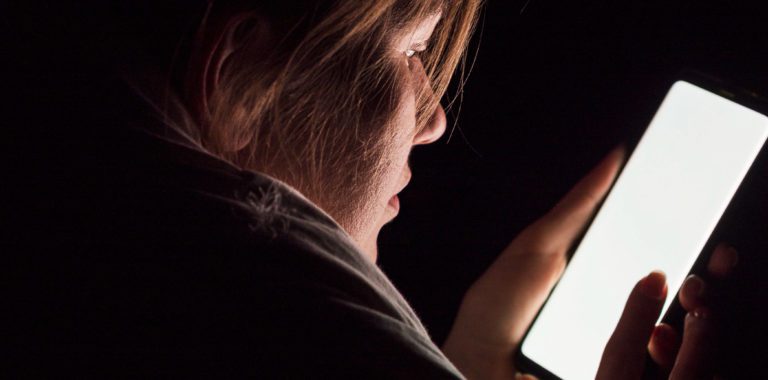 Close-up of a woman's hands holding a phone, illuminated by the screen in darkness