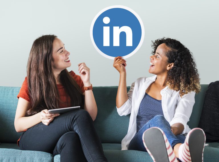Two joyful and relaxed young girls sitting on a green sofa, both looking up at a large LinkedIn logo